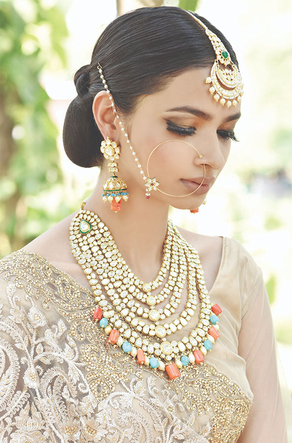 A woman in traditional attire wears elaborate gold jewelry, including a multi-layered necklace and ornate earrings, with a serene expression.